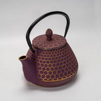 Close-up of purple cast iron teapot with honeycomb texture and black curved handle on white background