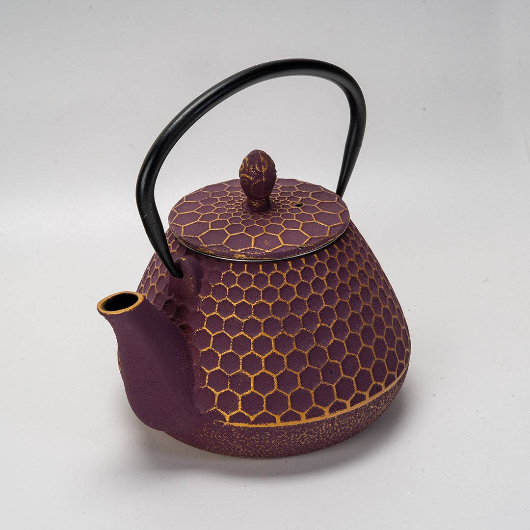 Close-up of purple cast iron teapot with honeycomb texture and black curved handle on white background