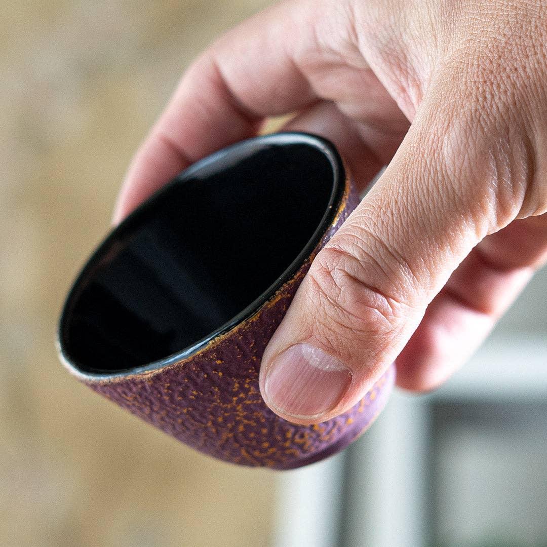 Hand holding a deep purple cast iron cup with honeycomb texture and glossy black interior close-up