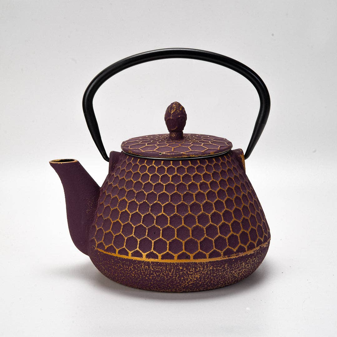 Deep purple cast iron teapot with honeycomb texture, curved spout, and black handle on a white background.