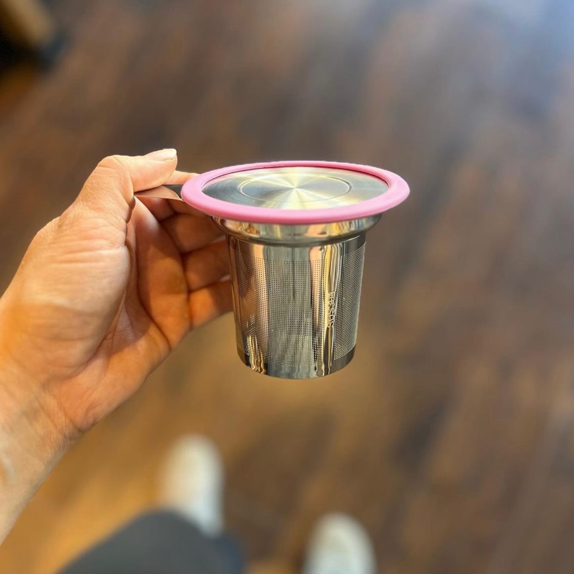 Close-up of Premium Tea Basket Infuser with pink rim and fine stainless steel mesh held over wooden floor background
