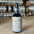 Dark glass tincture bottle of Defense Immunity blend with dropper on wooden surface and shelves in background