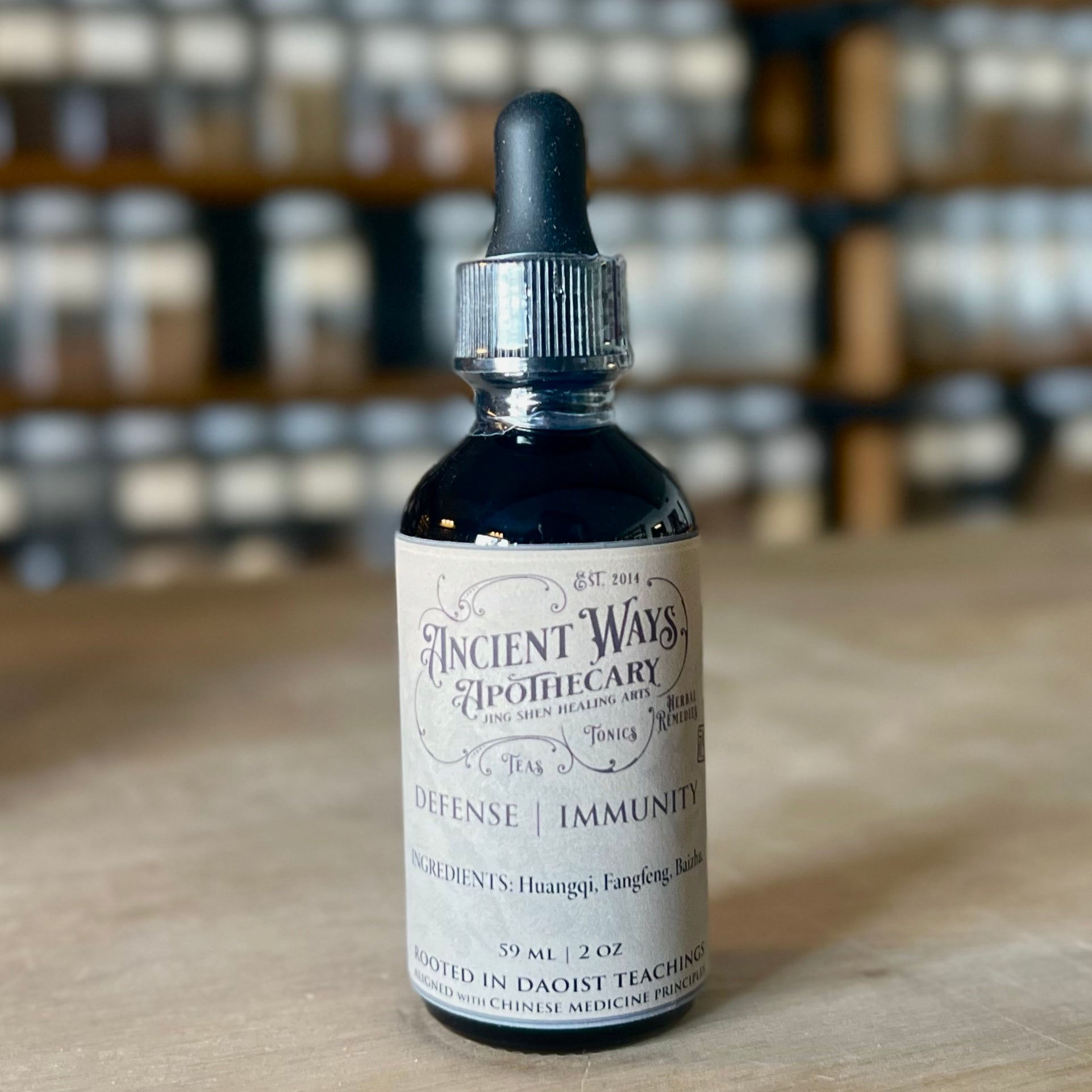 Dark glass tincture bottle of Defense Immunity blend with dropper on wooden surface and shelves in background