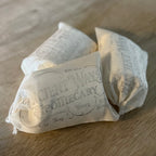Three cotton loose leaf tea filter bags with vintage apothecary-style text, resting on a wooden surface.