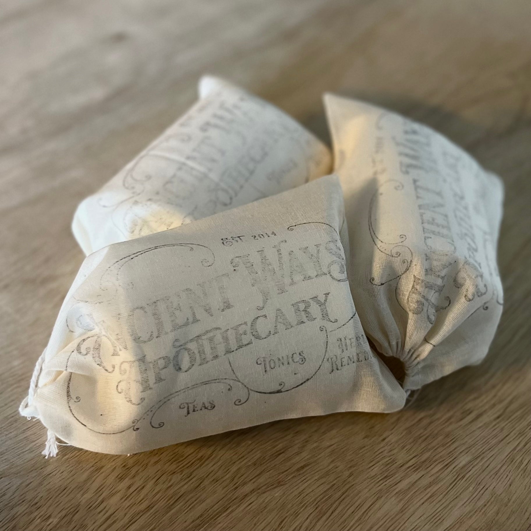 Three cotton loose leaf tea filter bags with vintage apothecary-style text, resting on a wooden surface.