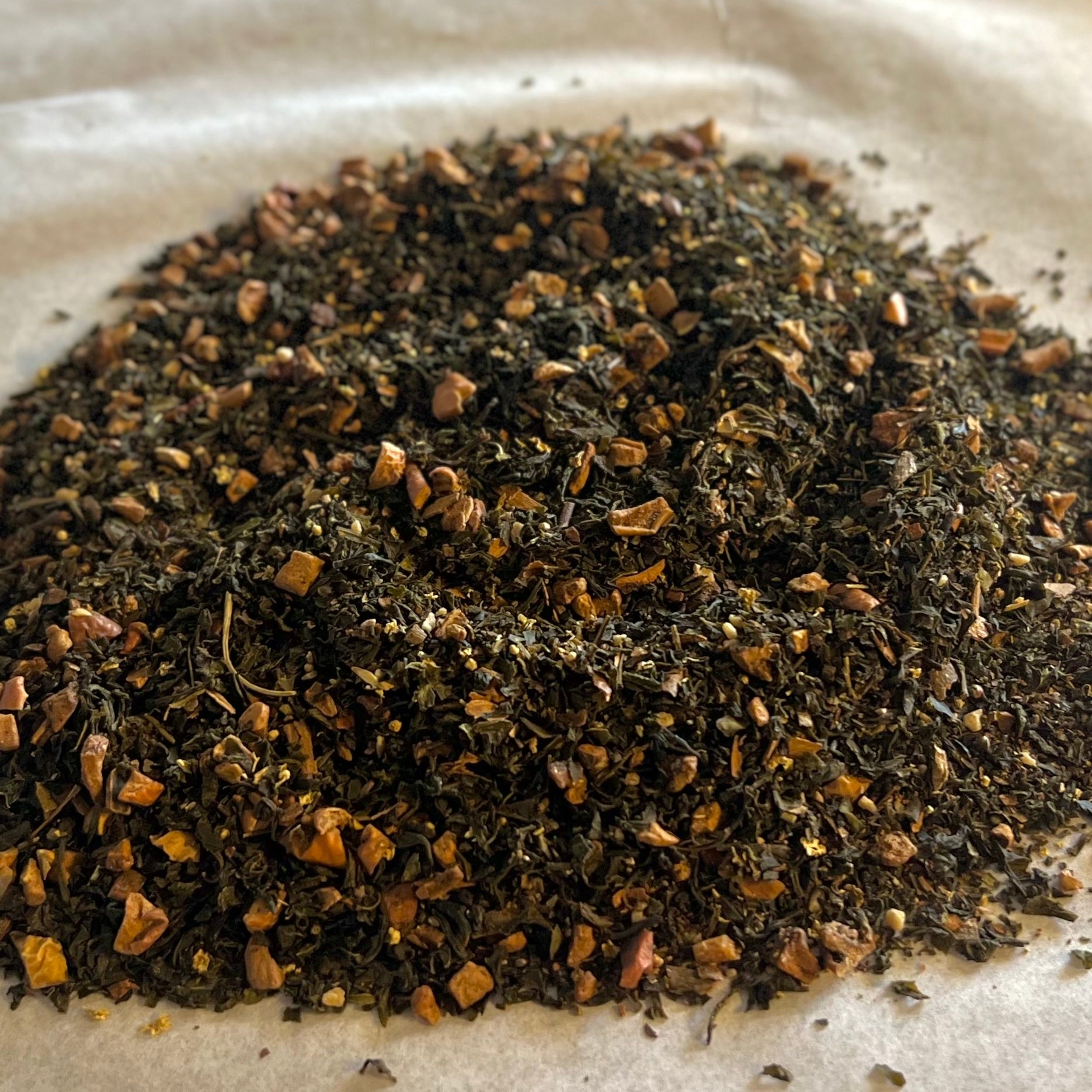 Loose Apple Crisp green tea blend with dried apple pieces and warming spices on parchment paper close-up