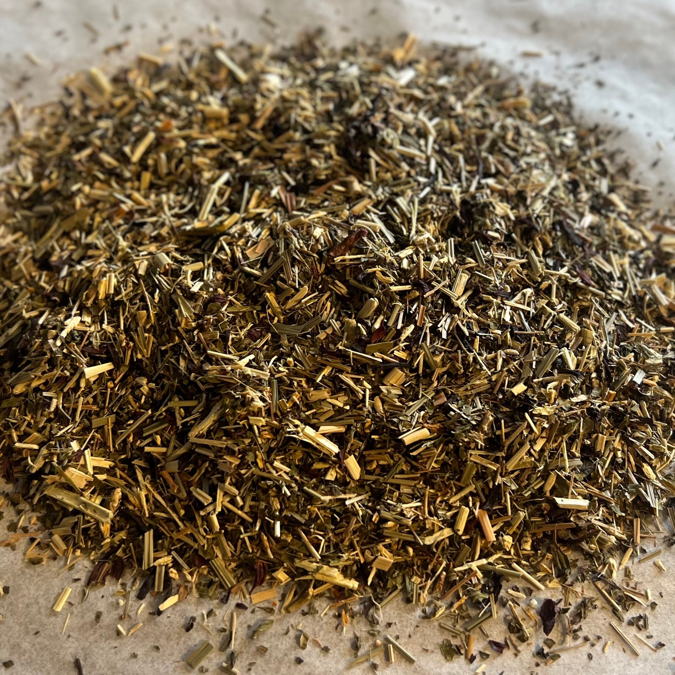 Close-up of Awaken & Flourish loose herbal tea blend with mixed dried botanicals and herbs on parchment paper.