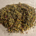 Close-up of loose Balance HER herbal tea blend with dried chamomile, peppermint, rose petals, and green leafy herbs on parchment paper
