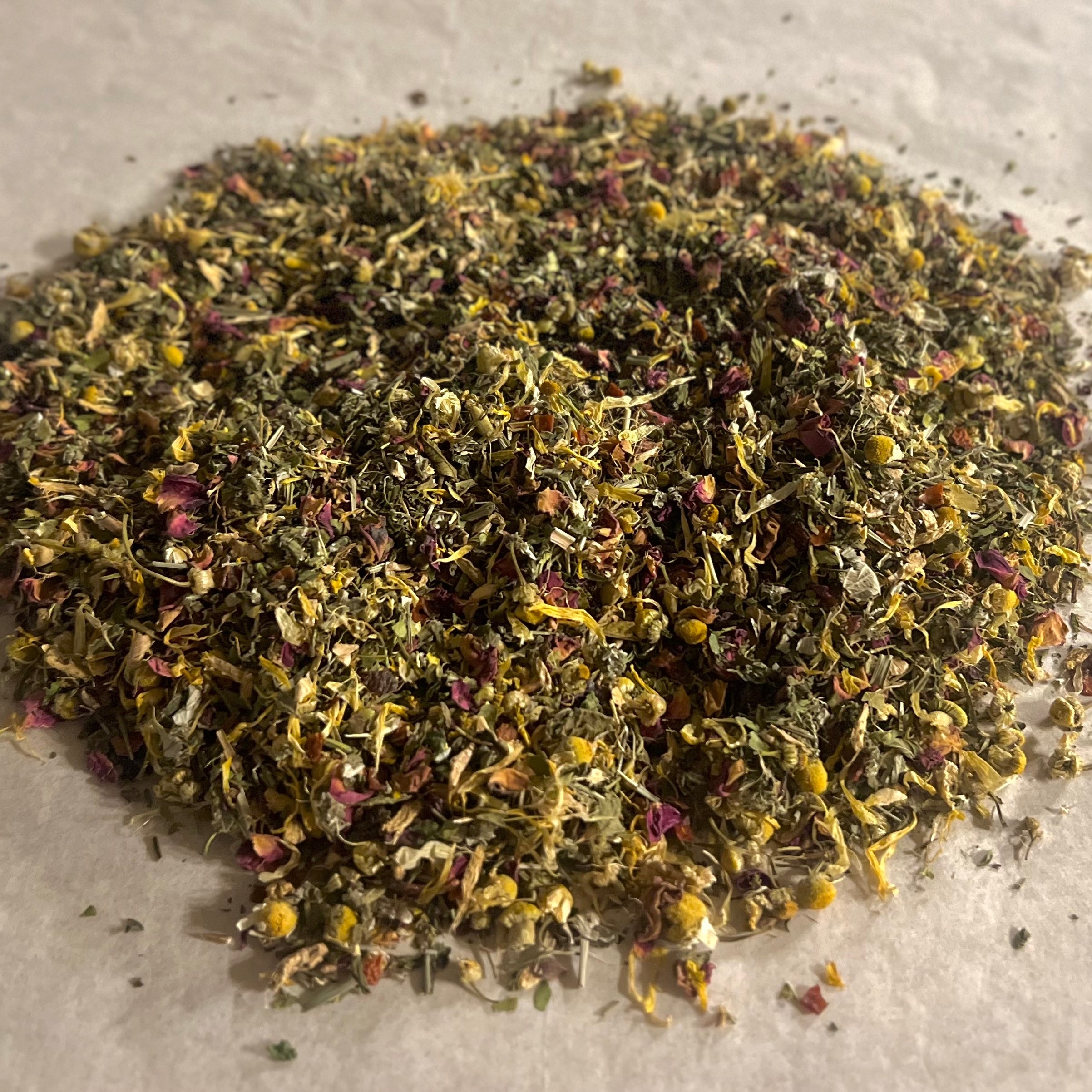 Close-up of loose Balance HER herbal tea blend with dried chamomile, peppermint, rose petals, and green leafy herbs on parchment paper