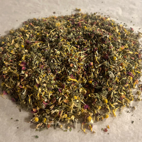 Close-up of loose Balance HER herbal tea blend with dried chamomile, peppermint, rose petals, and green leafy herbs on parchment paper