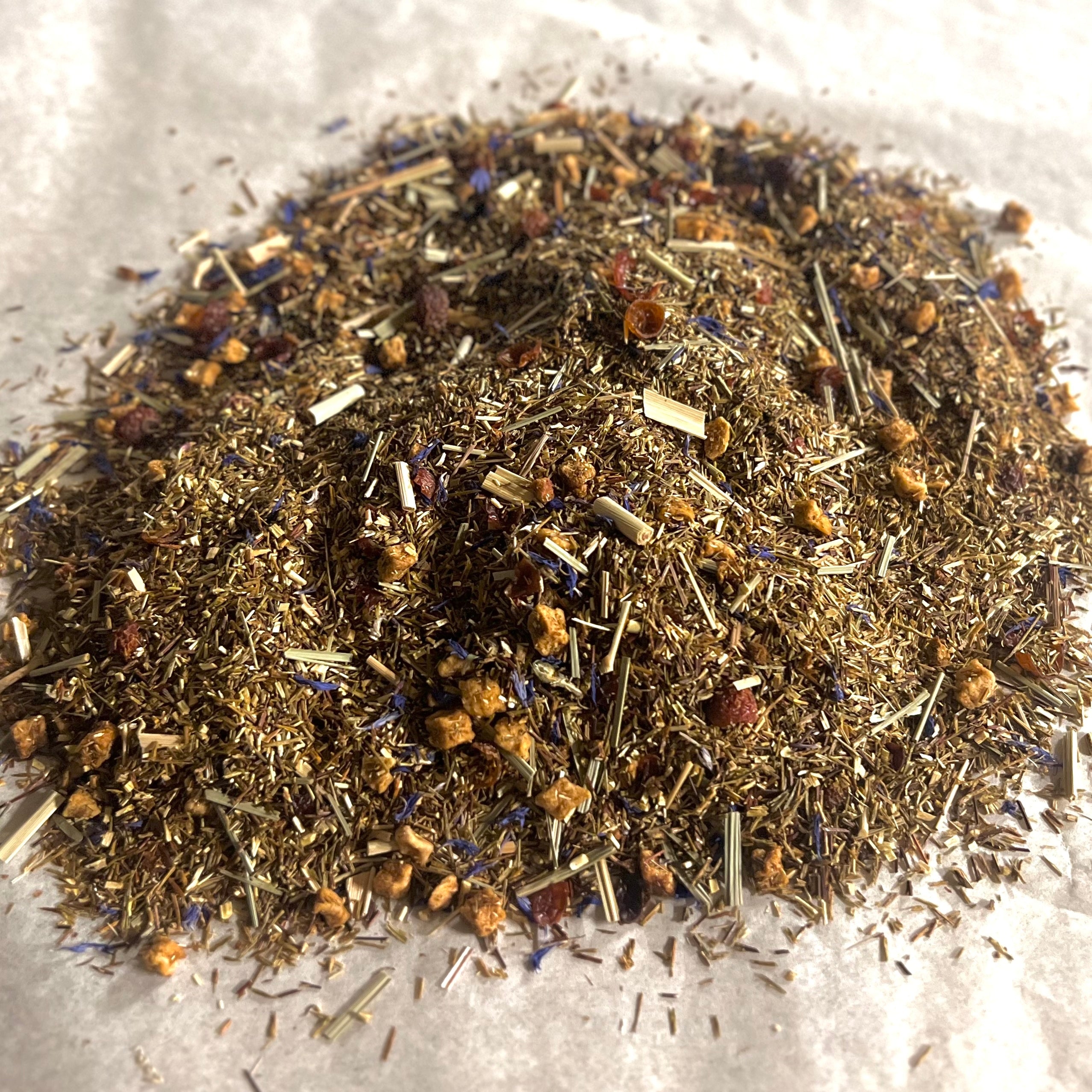 Close-up of loose Banana Berry Rooibos tea blend with green rooibos, strawberry pieces, and banana bits on parchment paper