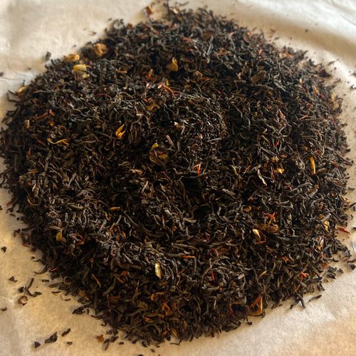 Close-up of loose Earl Grey tea blend with dark black tea leaves and hints of orange and red flower petals on parchment paper