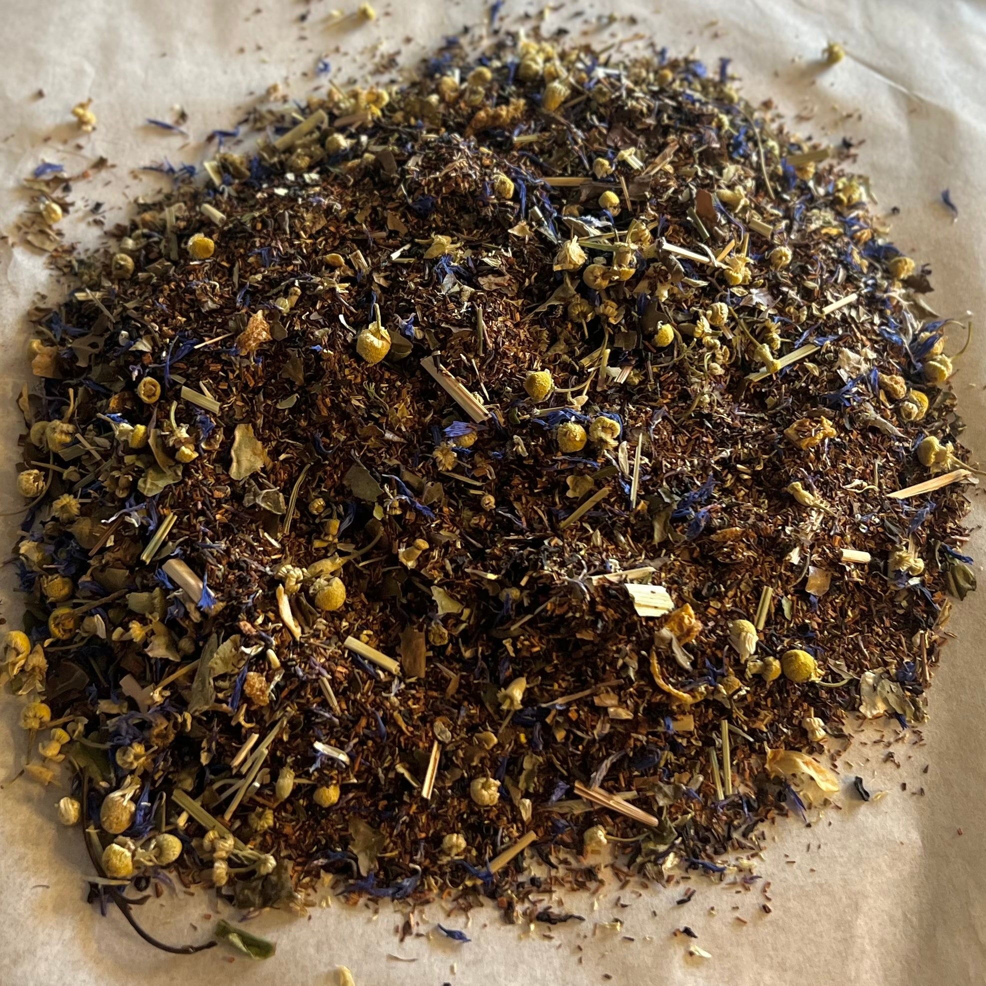 Loose blend of Big Citrus Skies tea with rooibos, black tea, orange zest, lemongrass, and chamomile flowers on paper background