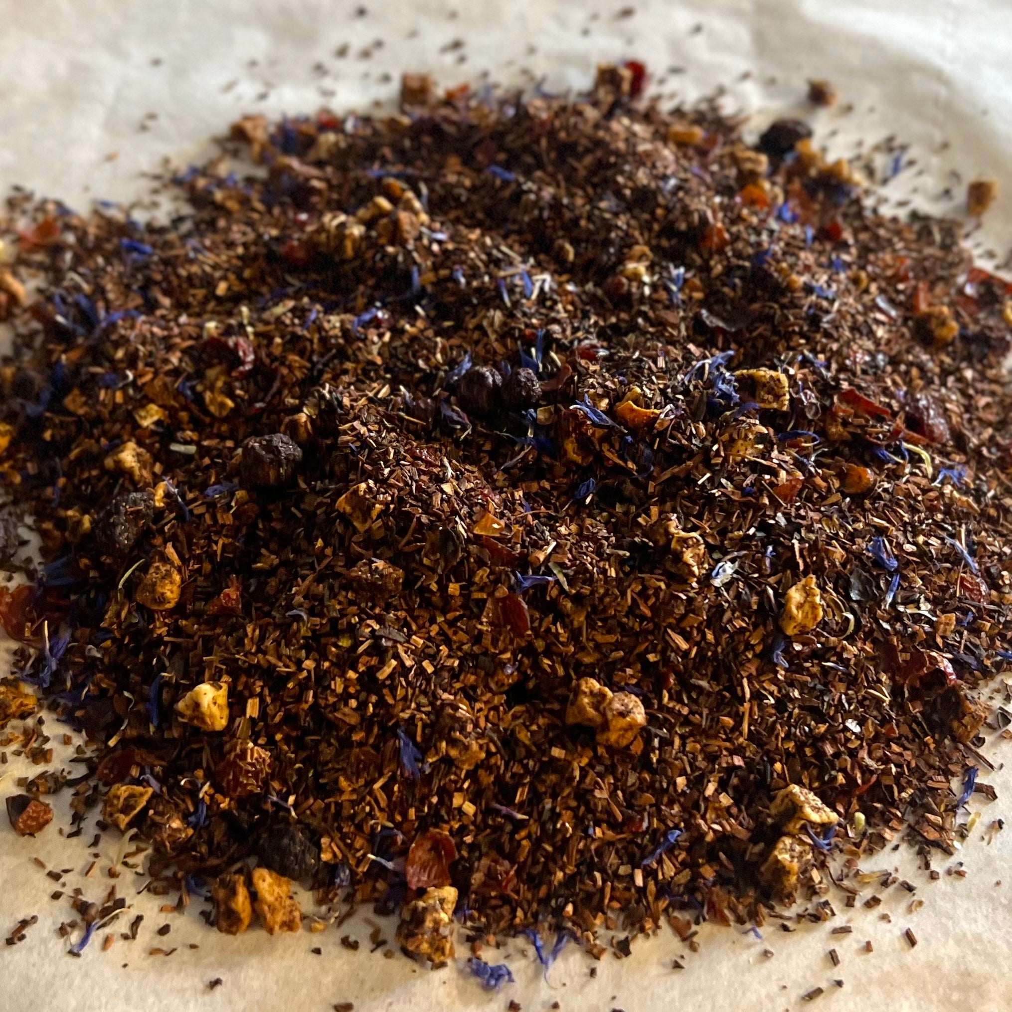 Close-up of Blueberry Shortstack loose tea blend with honeybush, rose hips, apple pieces, and blue flower petals on parchment paper