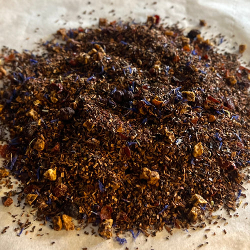 Close-up of Blueberry Shortstack loose tea blend with honeybush, rose hips, apple pieces, and blue flower petals on parchment paper