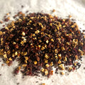 Close-up of loose In Full Bloom sampler tea blend with dried fruit pieces, hibiscus, and floral botanicals on light surface