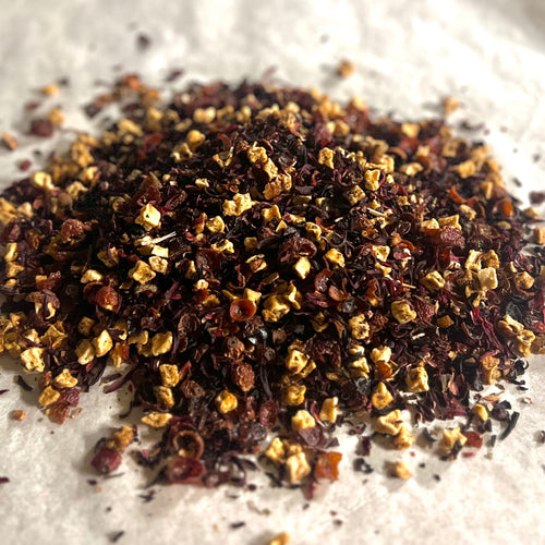 Close-up of loose In Full Bloom sampler tea blend with dried fruit pieces, hibiscus, and floral botanicals on light surface