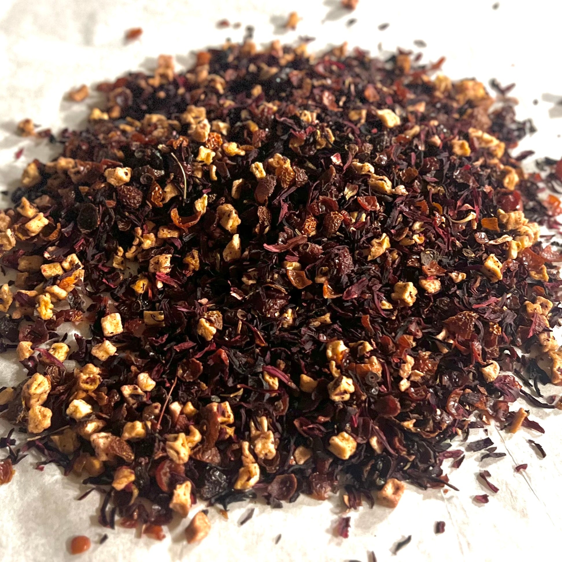 Close-up of Cherry, Cherry, Cherry herbal tea blend with dried cherries, hibiscus petals, and fruit pieces on a white surface