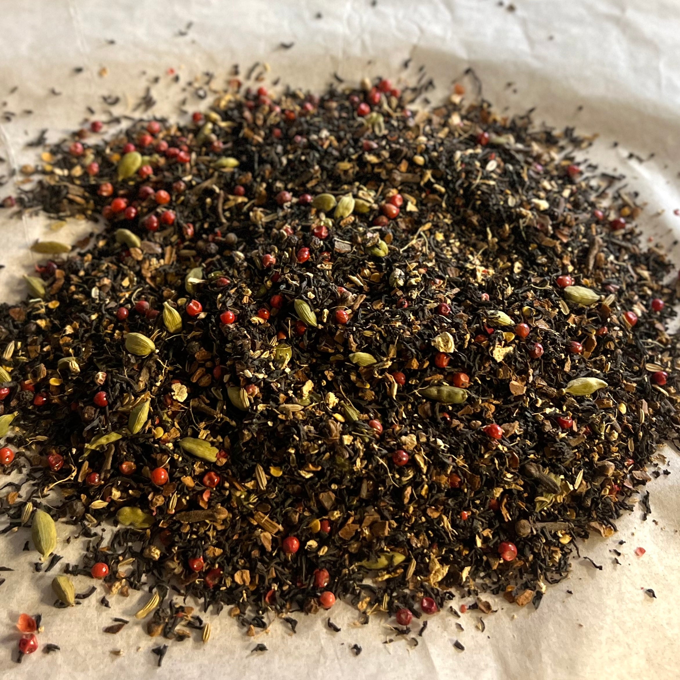 Close-up of Chai No. 79 loose tea blend with black tea, cardamom, red peppercorns, and warming chai spices on parchment paper