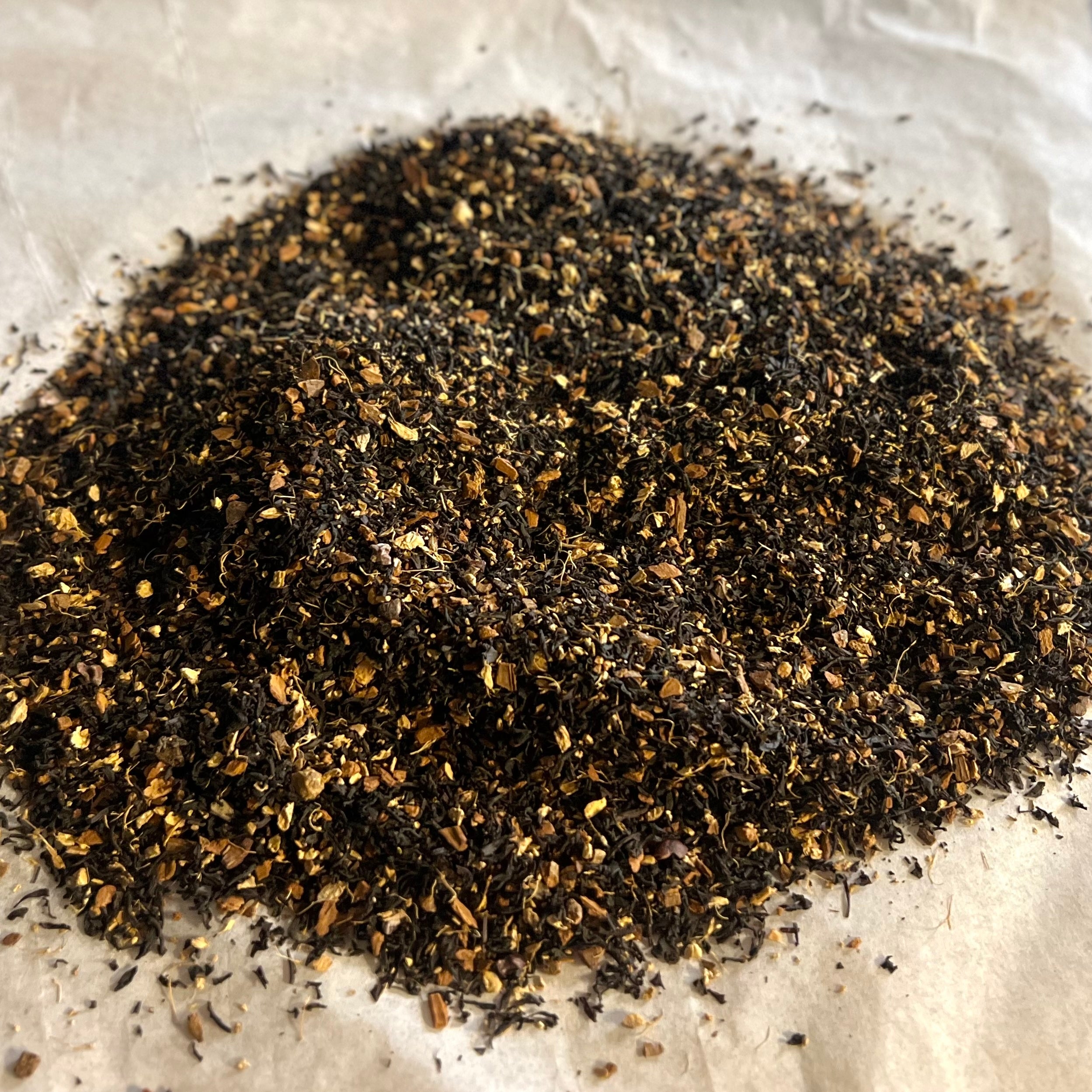 Close-up of Chai No. 71 loose tea blend with black tea, cinnamon, ginger, and cocoa nibs on parchment paper.