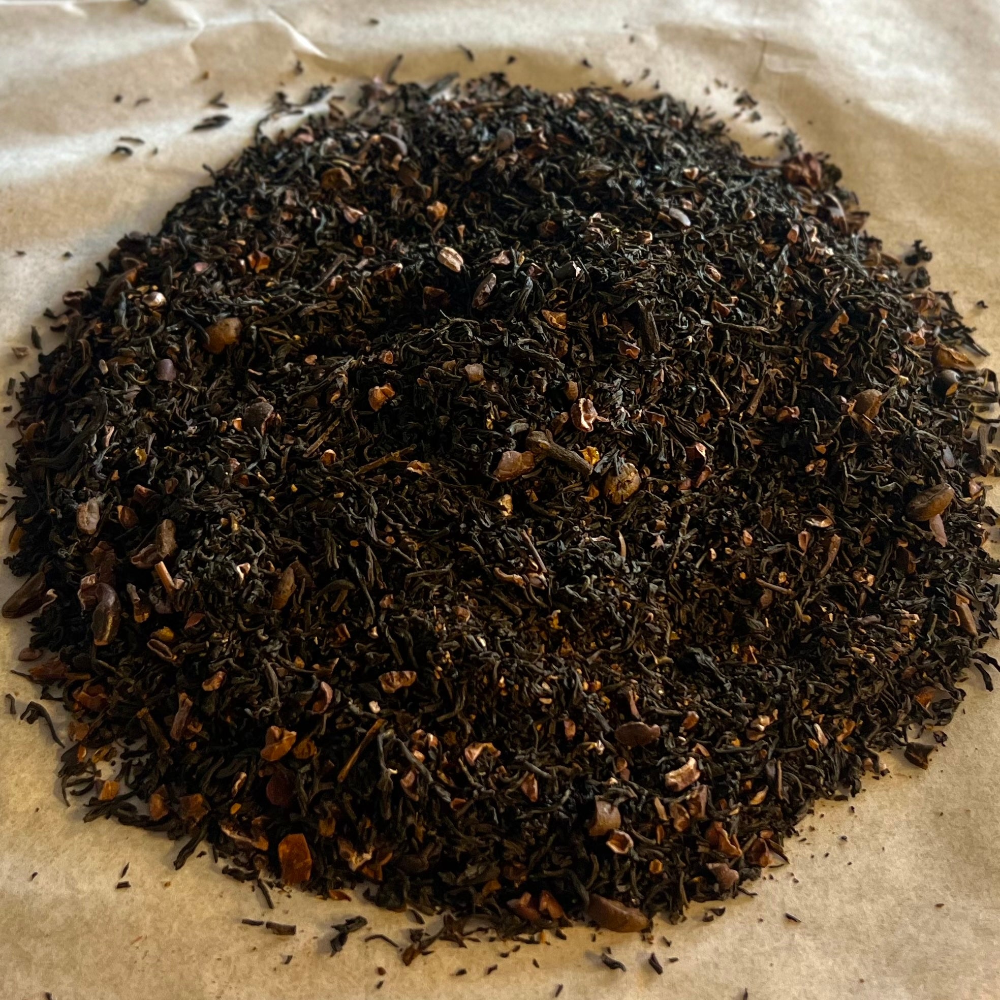 Close-up of Colombian Mocha loose tea blend with black tea leaves, cacao husks, and coffee beans on parchment paper.