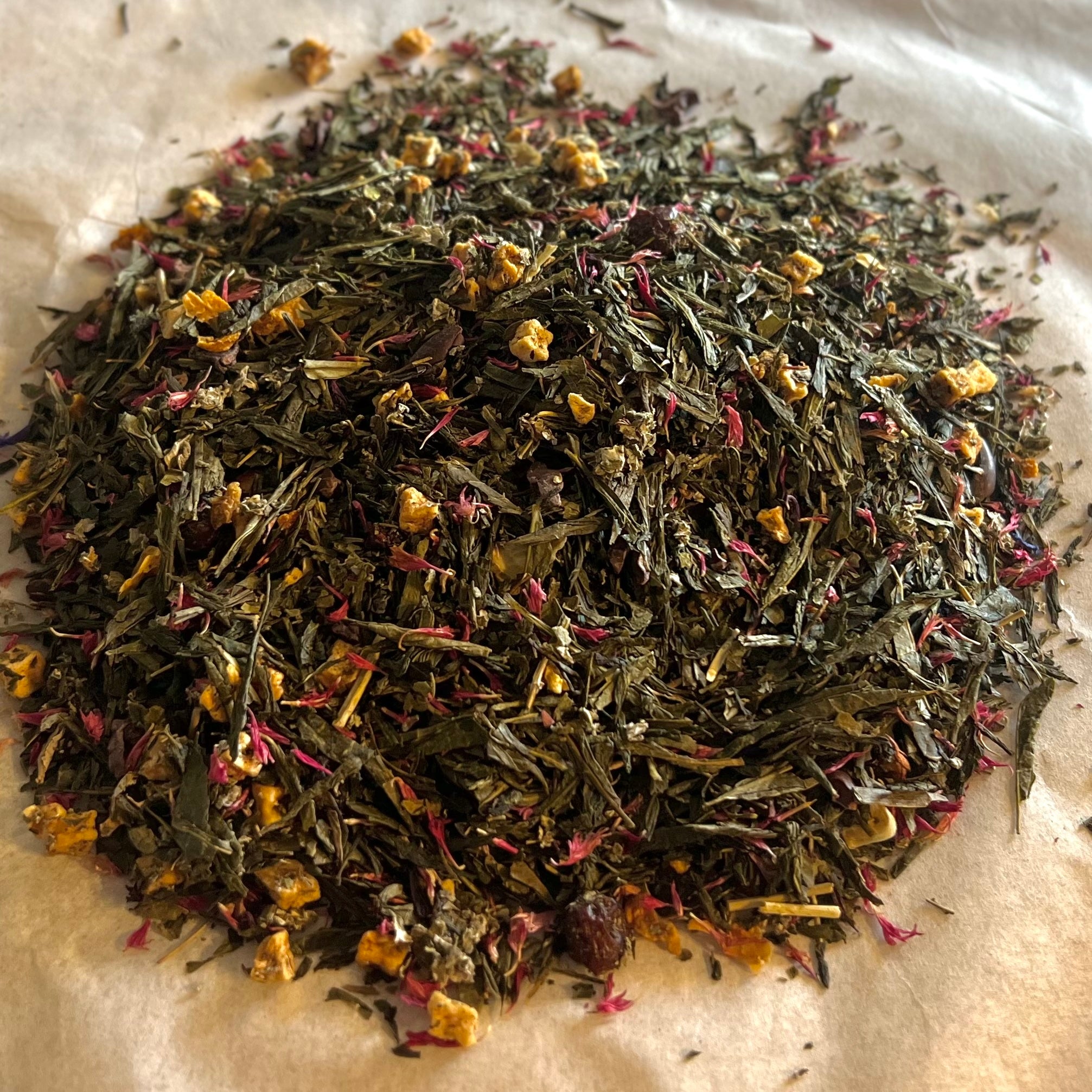 Close-up of Cranberry Muffin loose green tea blend with tart cranberries, cocoa nibs, apple pieces, and orange zest on parchment paper.