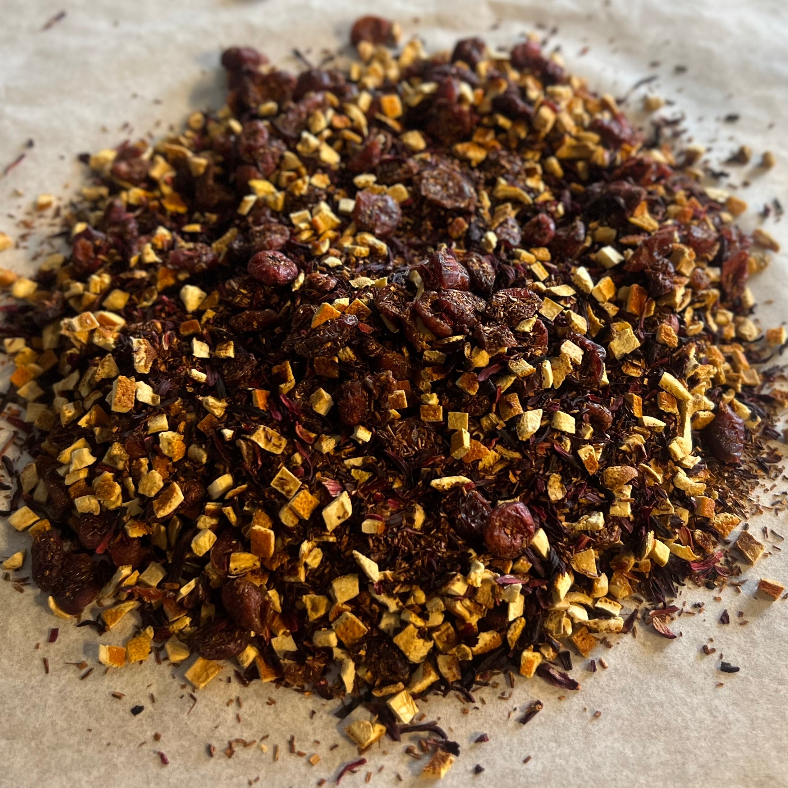 Close-up of Cranberry Sunset rooibos tea blend with dried cranberries and orange peel pieces on parchment paper