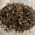 Close-up of loose Elderberry Blend herbal tea with hibiscus, rose hips, elderberry, echinacea, and apple pieces on white surface
