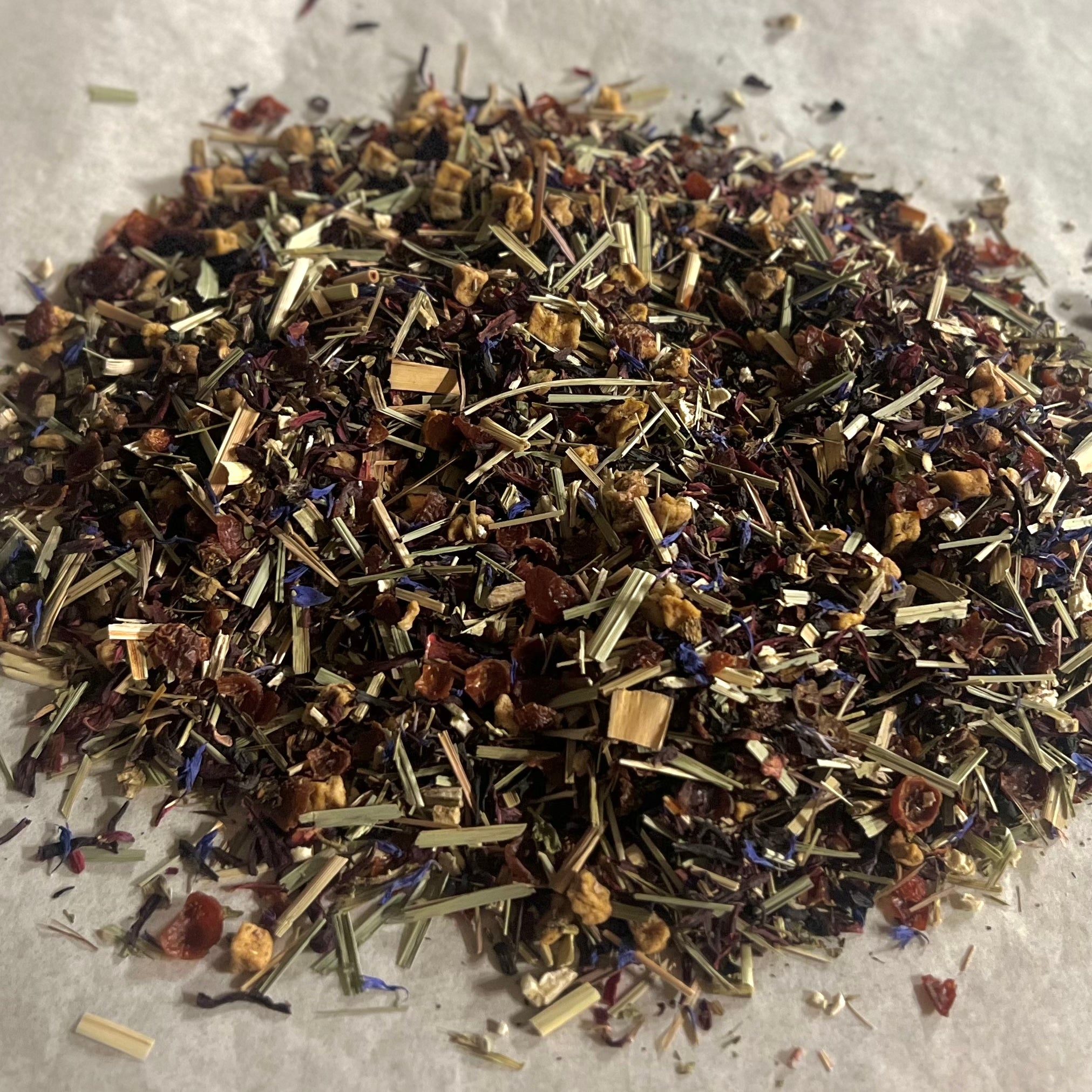 Close-up of loose Elderberry Blend herbal tea with hibiscus, rose hips, elderberry, echinacea, and apple pieces on white surface