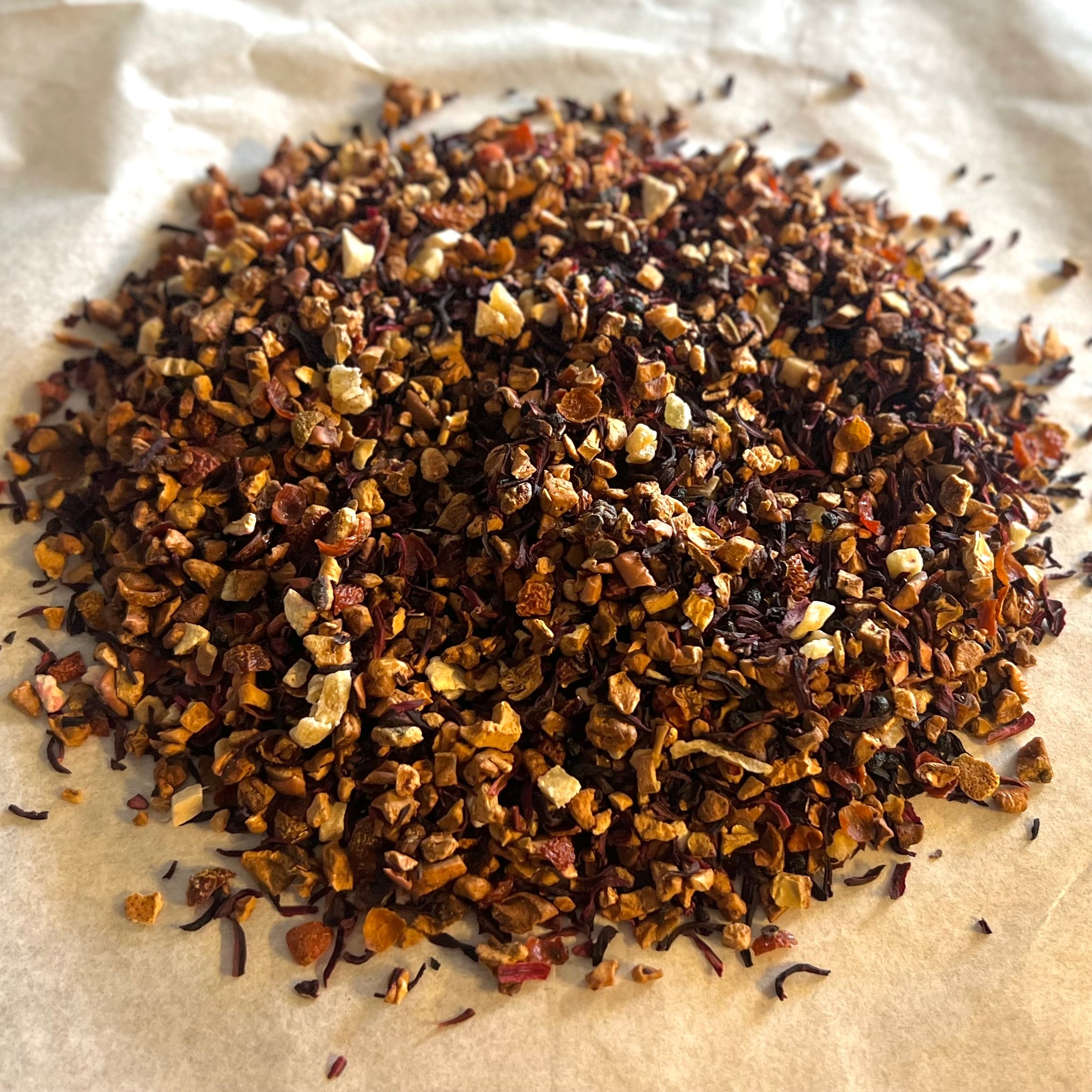 Close-up of Elderberry Island Twist loose tea blend with dried elderberry, apple, hibiscus, rosehip, mango, pineapple, and orange pieces on parchment.