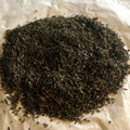 Loose blend of Fields of Raspberry tea with sencha green tea leaves and small dried raspberry pieces on brown paper.