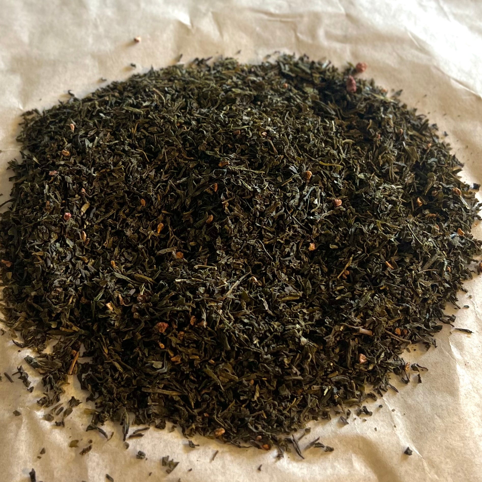 Loose blend of Fields of Raspberry tea with sencha green tea leaves and small dried raspberry pieces on brown paper.