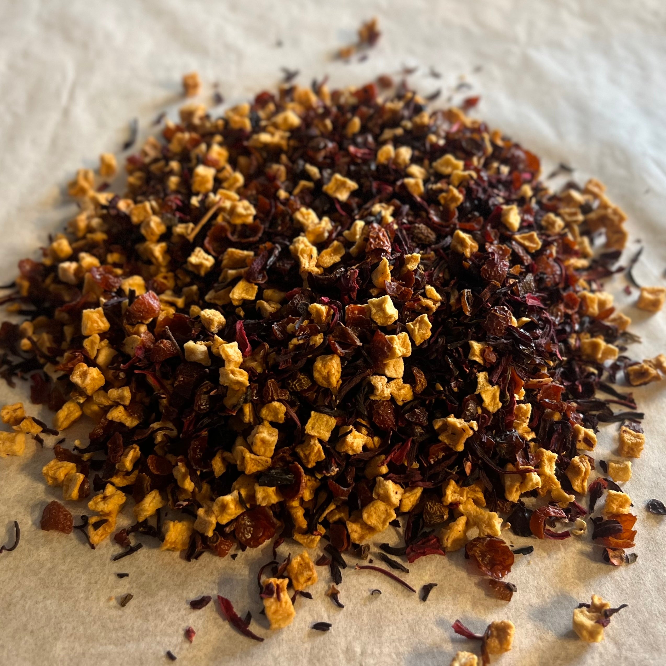 Close-up of loose Crisp Mornings & Cozy Mugs tea sampler blend with dried apple pieces and hibiscus petals on parchment paper.