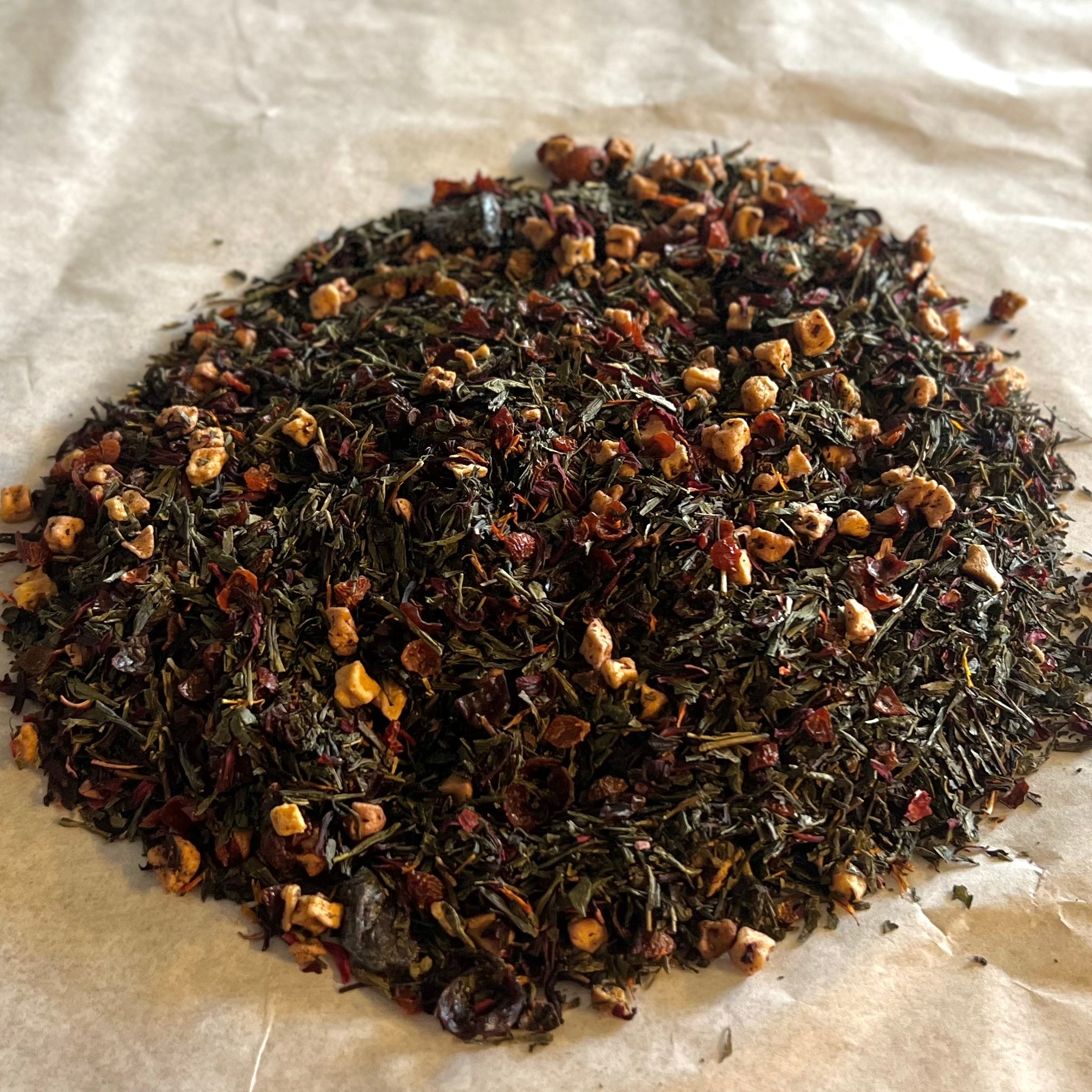 Loose Flathead Cherry Goodness tea blend with dark green Sencha leaves and dried cherry pieces on parchment paper
