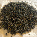 Close-up of rolled Fujian Orchid Oolong tea leaves, showing dark green and brown hues on parchment paper.
