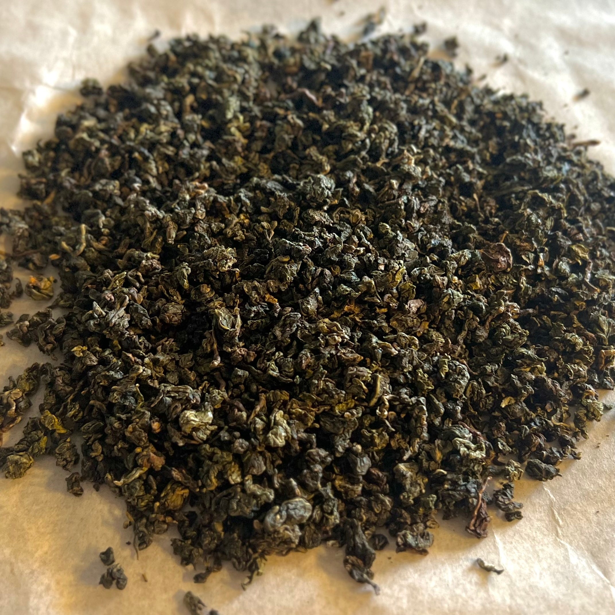 Close-up of rolled Fujian Orchid Oolong tea leaves, showing dark green and brown hues on parchment paper.