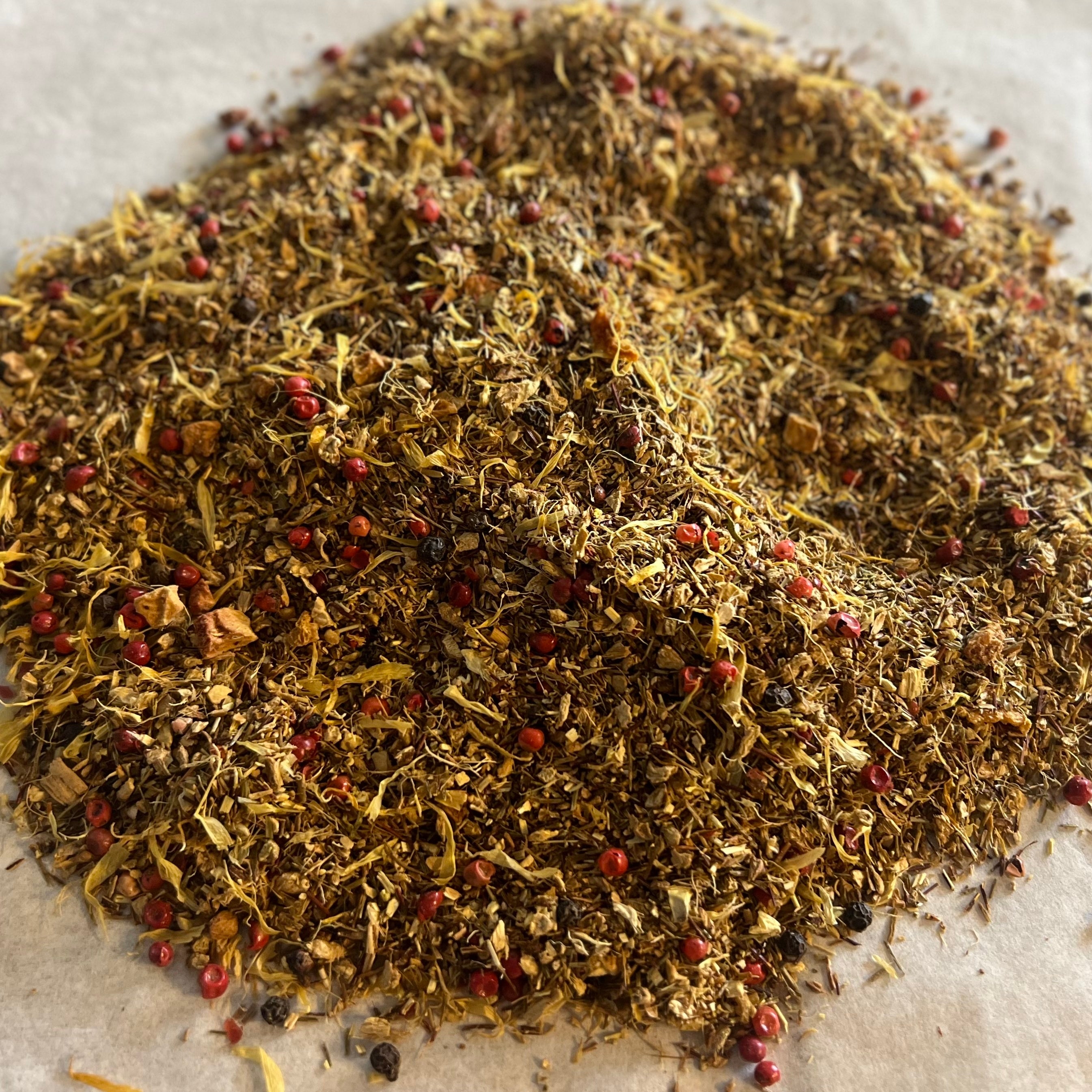 Loose Ginger Sunrise tea blend with green rooibos, dried ginger pieces, peppercorns, and golden flower petals on parchment paper.
