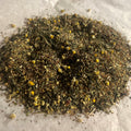 Close-up of Go w/The Flow loose herbal tea blend with chamomile flowers and delicate dried leaves on white parchment surface