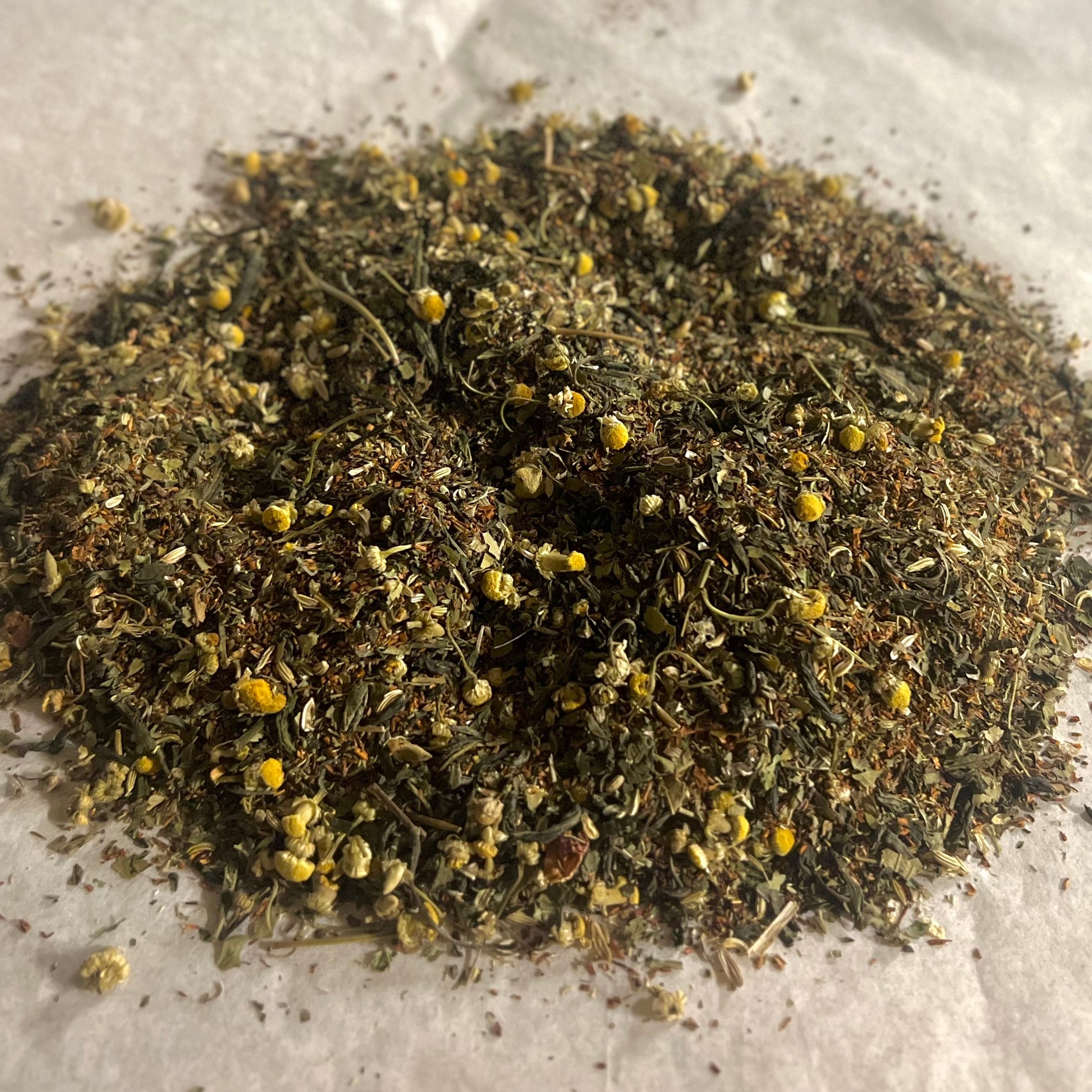 Close-up of Go w/The Flow loose herbal tea blend with chamomile flowers and delicate dried leaves on white parchment surface