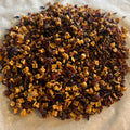Close-up of Groves of Sunshine caffeine-free tea blend with dried apple, hibiscus, ginger, and cinnamon pieces on parchment paper