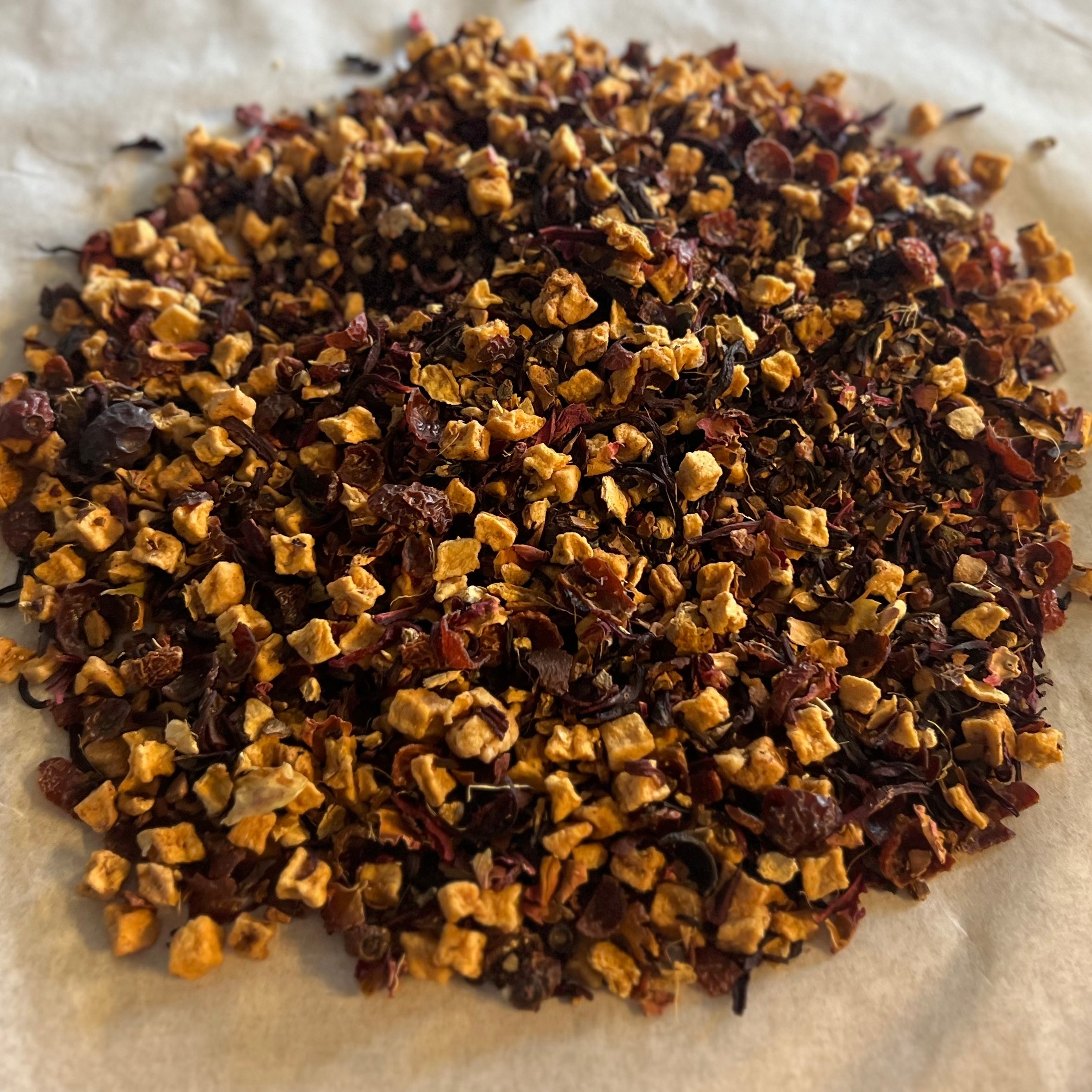 Close-up of Groves of Sunshine caffeine-free tea blend with dried apple, hibiscus, ginger, and cinnamon pieces on parchment paper