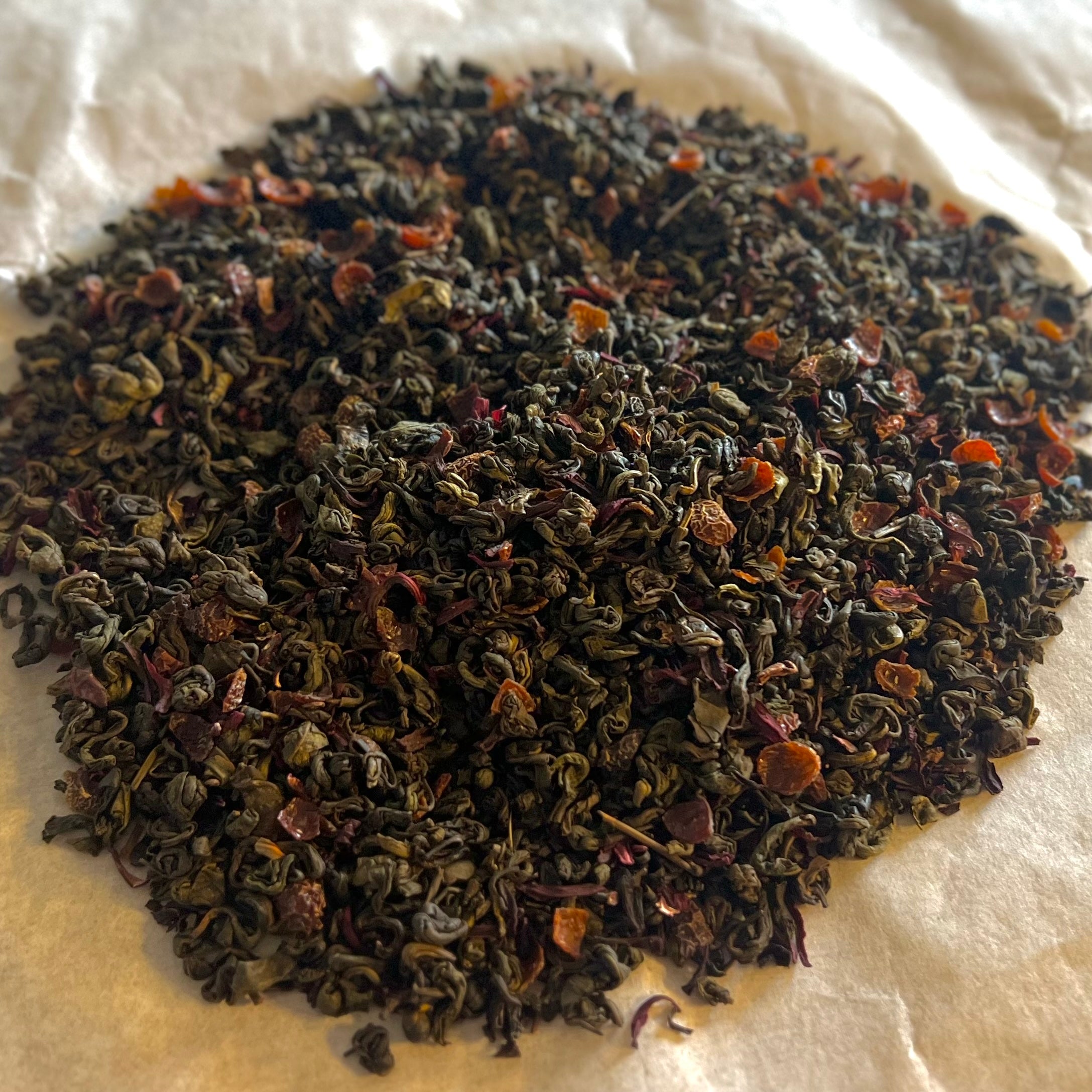 Close-up of loose Hibiscus Green Tea blend with green tea leaves and red hibiscus petals on white surface