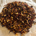 Close-up of loose Hibiscus Orange tea blend with dried hibiscus, rose hips, and orange peel on parchment paper