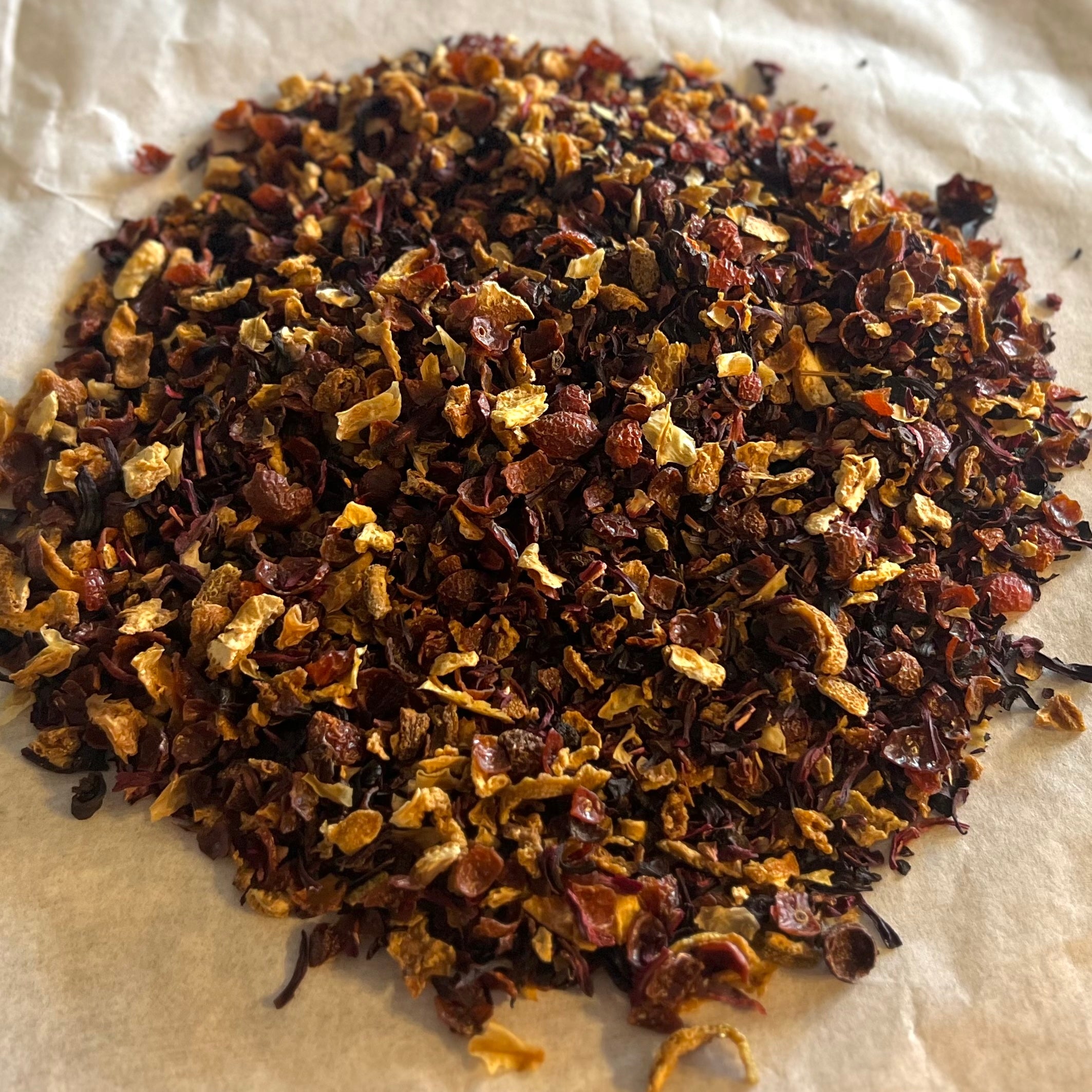 Close-up of loose Hibiscus Orange tea blend with dried hibiscus, rose hips, and orange peel on parchment paper