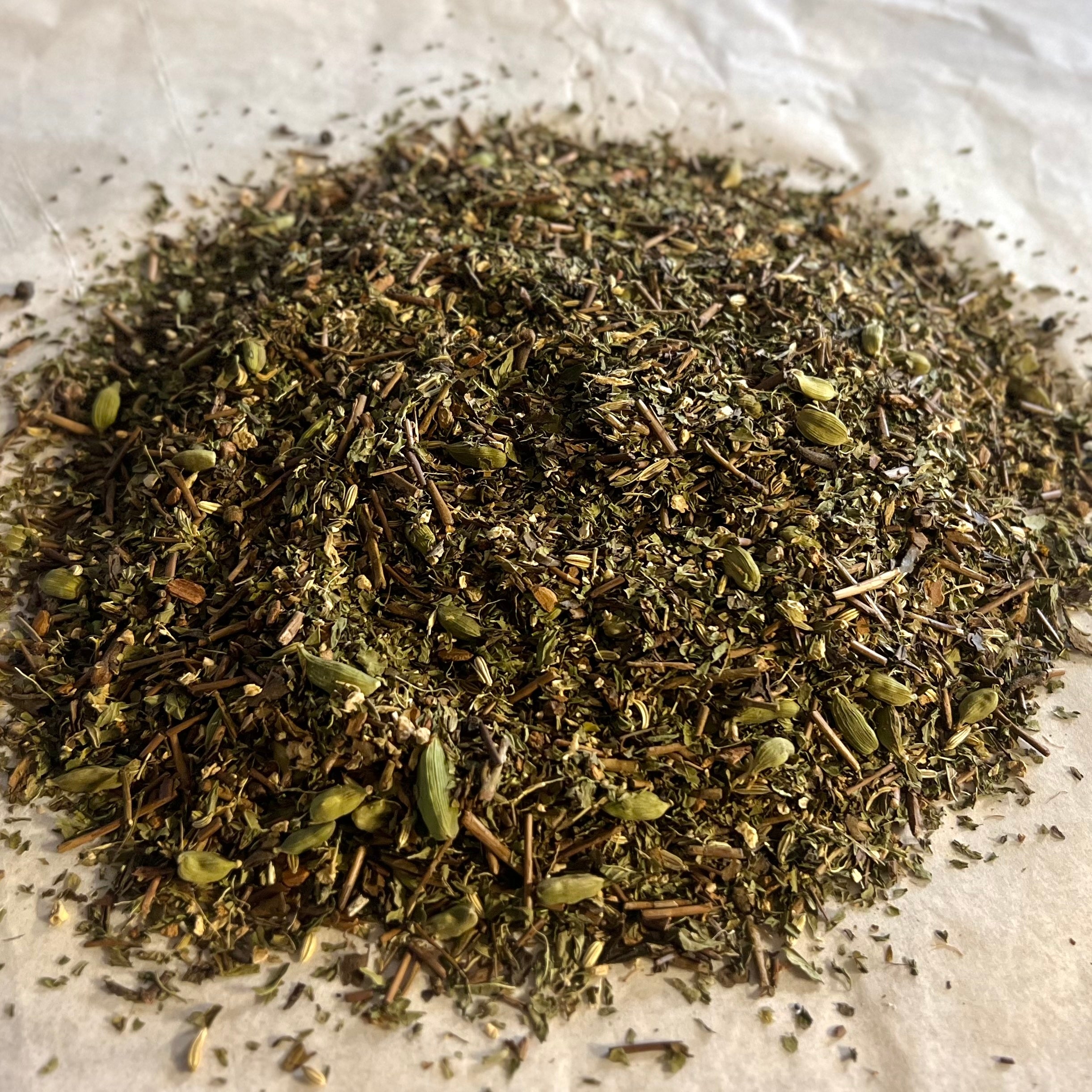 Close-up of Chai No. 74 loose tea blend with roasted green tea, spearmint, chai spices, and hojicha pieces on parchment paper