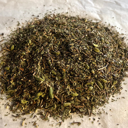 Close-up of Chai No. 74 loose tea blend with roasted green tea, spearmint, chai spices, and hojicha pieces on parchment paper