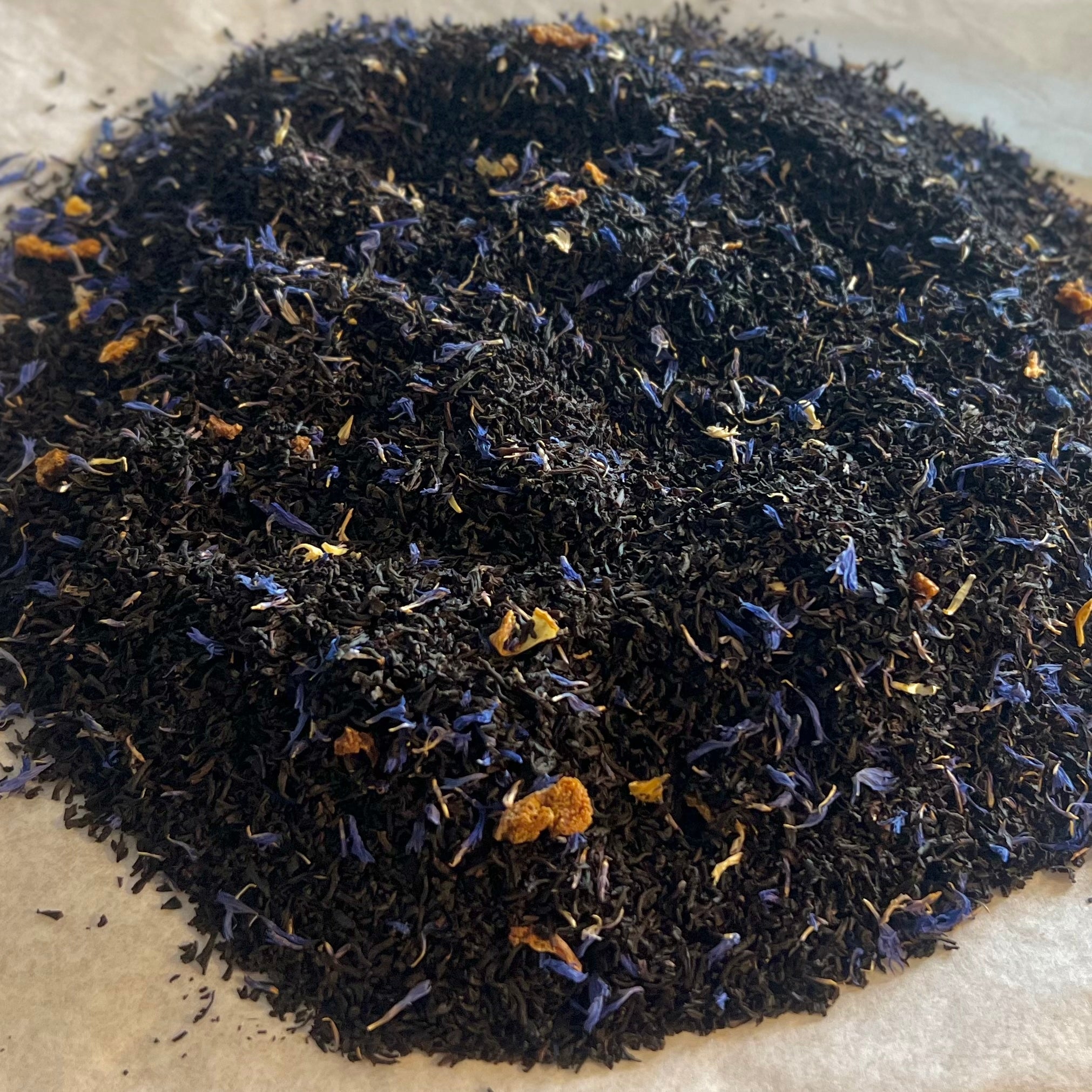 Close-up of loose Inner Courtyard Earl Grey black tea blend with bergamot and blue flower petals on parchment paper.
