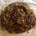 Loose Jasmine Rose tea blend with rooibos, black tea, wild rose buds, apple pieces, and delicate jasmine petals on parchment