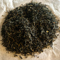 Close-up of Jasmine Yin Hao loose green tea leaves with delicate light tips on parchment paper background