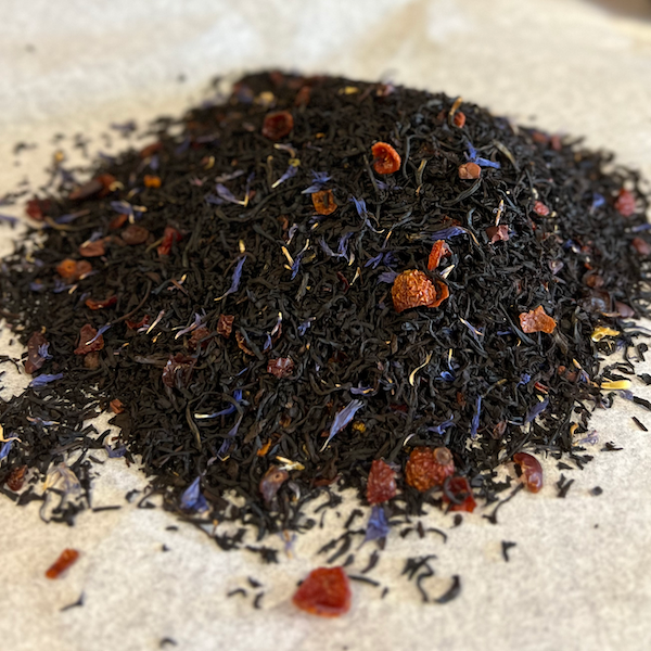 Close-up of Kentucky Barrel-Aged black tea blend with dark leaves, red berry pieces, and blue flower petals on parchment paper